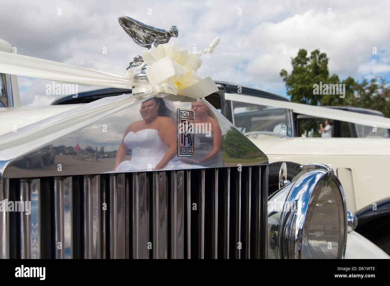 Horizontale Nahaufnahme der Geist der Ekstase Statue und Reflexion einer Braut und Brautjungfern im Grill eines Rolls Royce Oldtimer bei einer Hochzeit. Stockfoto