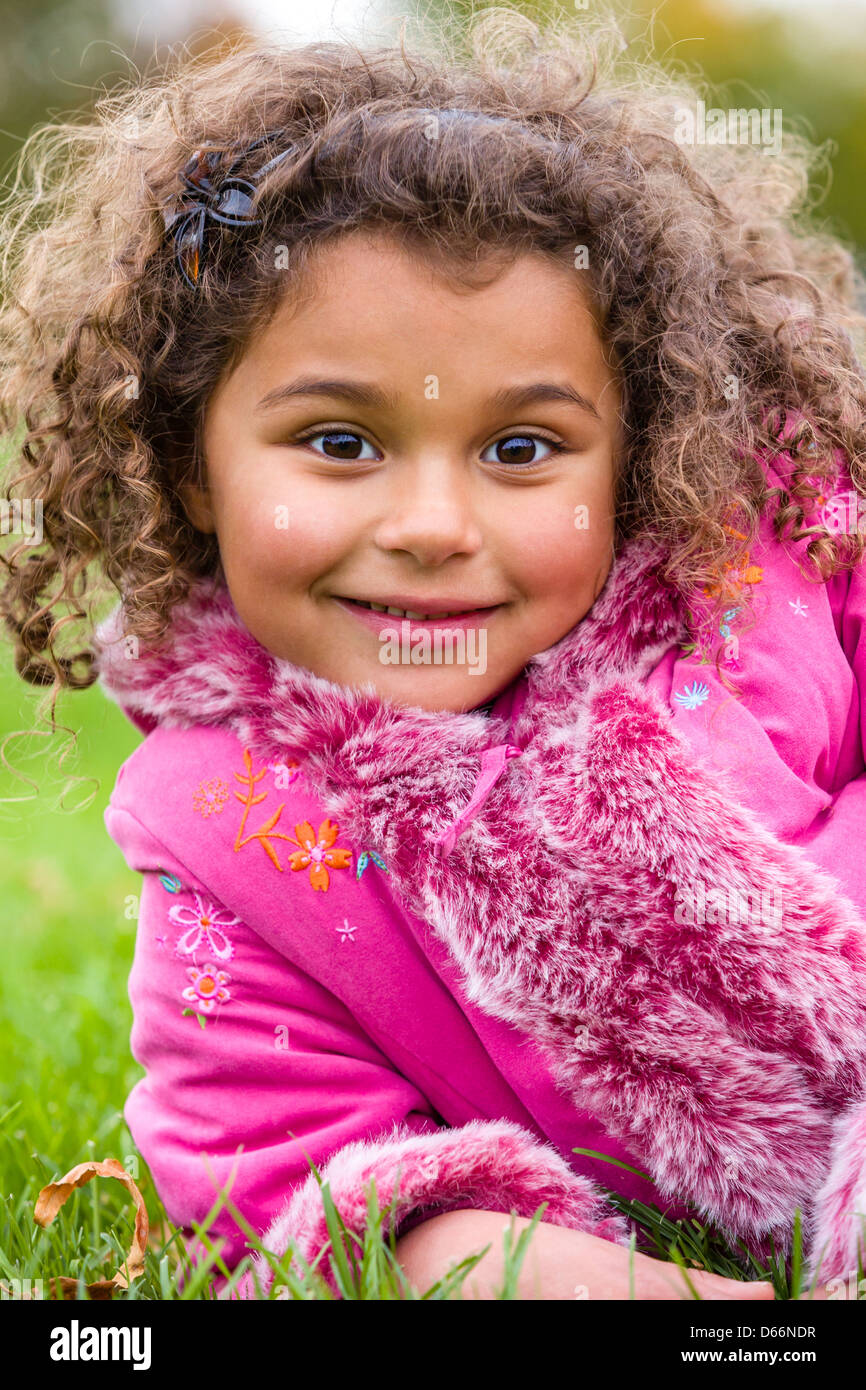 Junges Mädchen von gemischter Rasse mit lockigen Haaren, auf dem Gras liegend. Stockfoto
