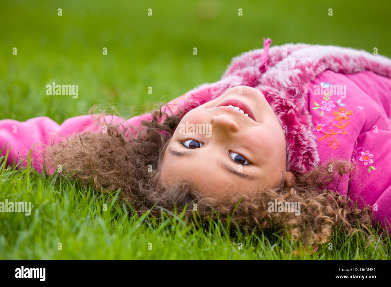 Junge Mädchen gemischter Rasse, in einem rosa Top, auf dem Gras liegend. Stockfoto