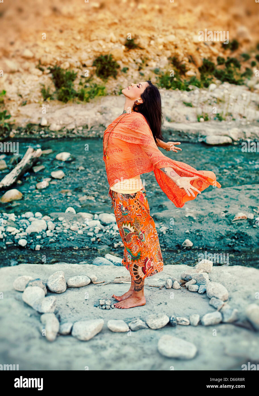 Frau im Freien in der Nähe eines Flusses mit ihren Armen und Herzen öffnen in ein Mandala aus Steinen. Stockfoto