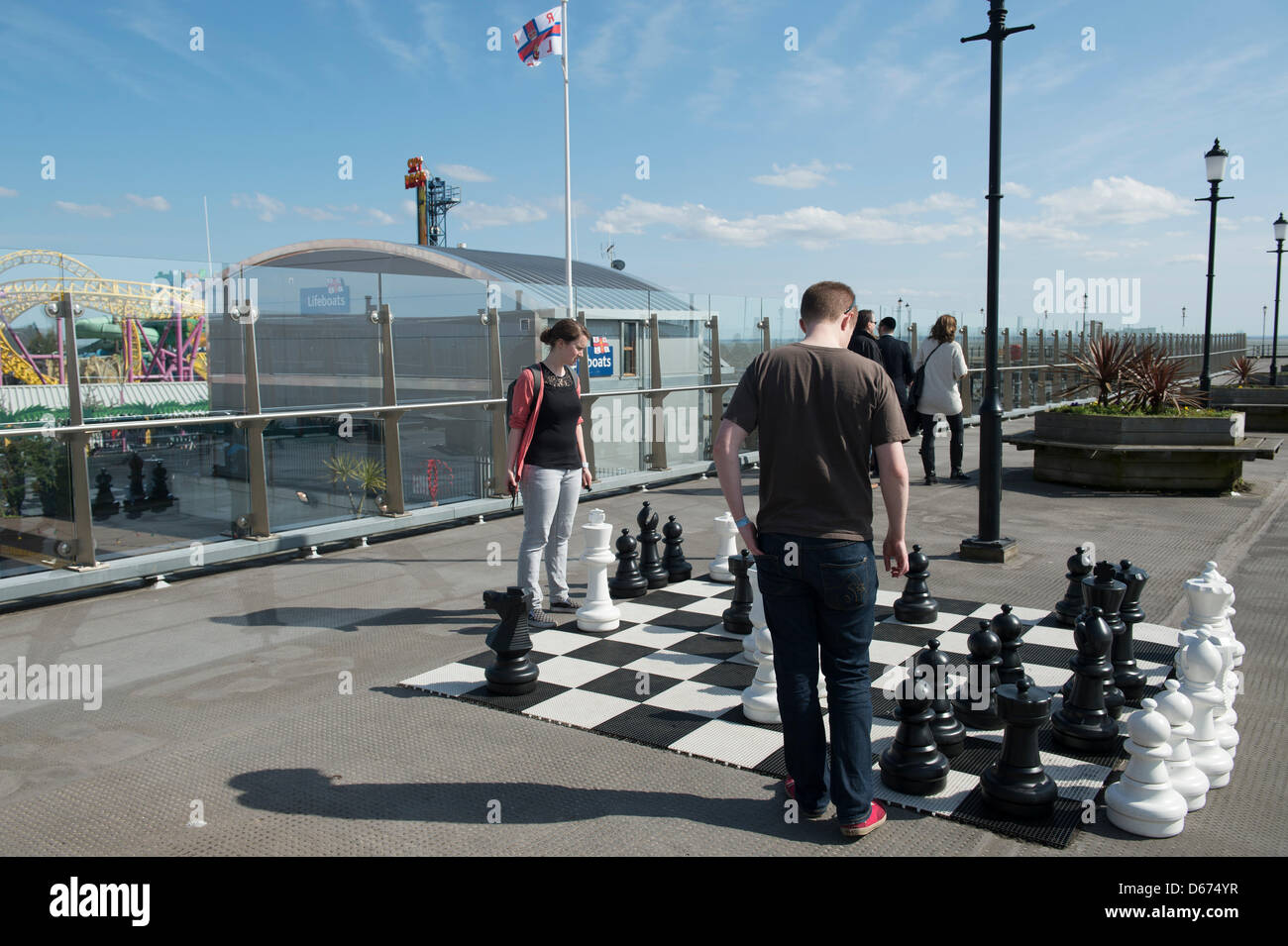 Ein junges Paar genießen das gute Wetter, da sie über große Schach zu Beginn des Southend Pier, in Essex, England spielen. Stockfoto