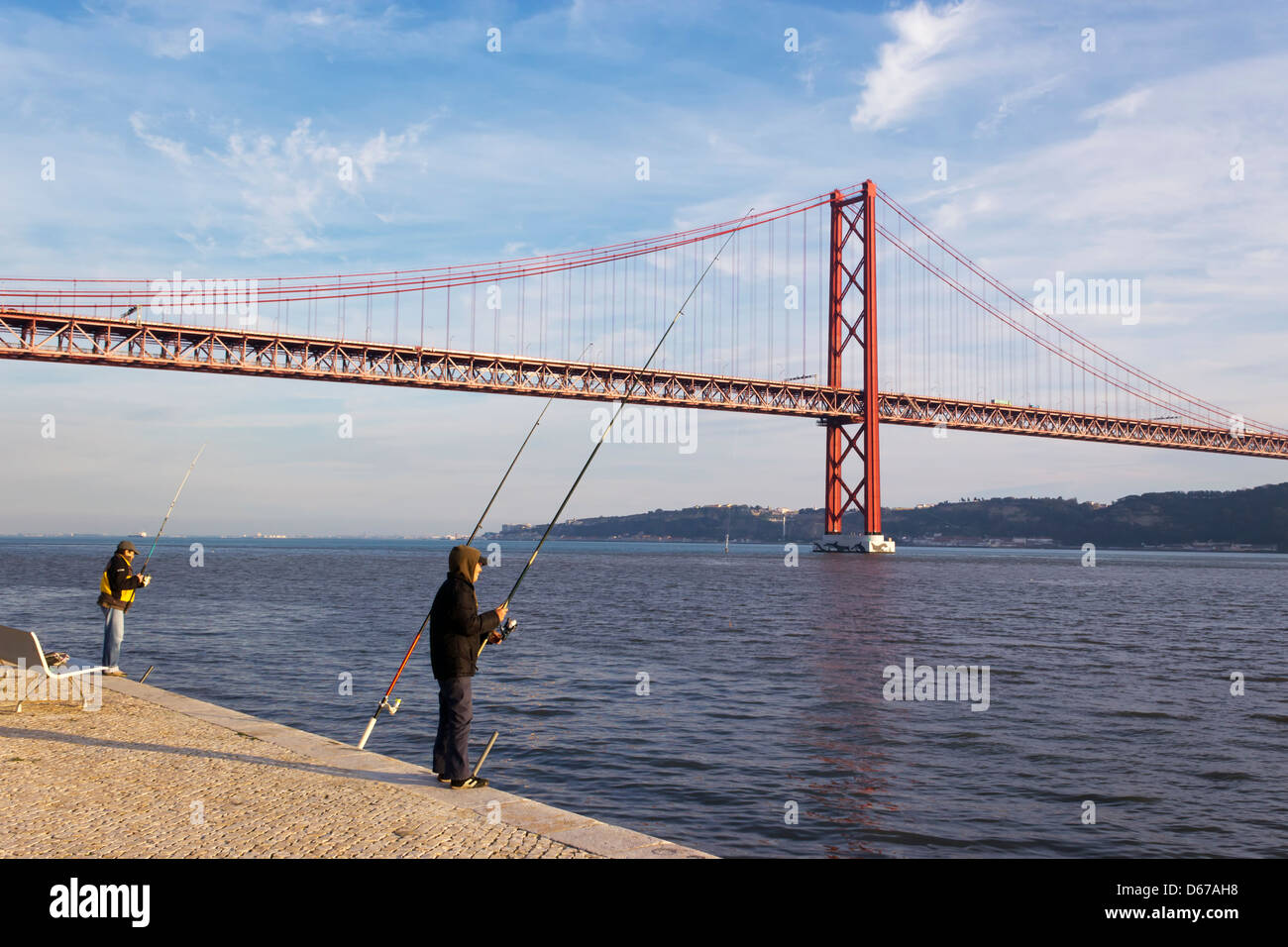 Lissabon, Portugal. Fischer an der Seite des Tejo, die 25 de Abril Brücke im Hintergrund. Stockfoto