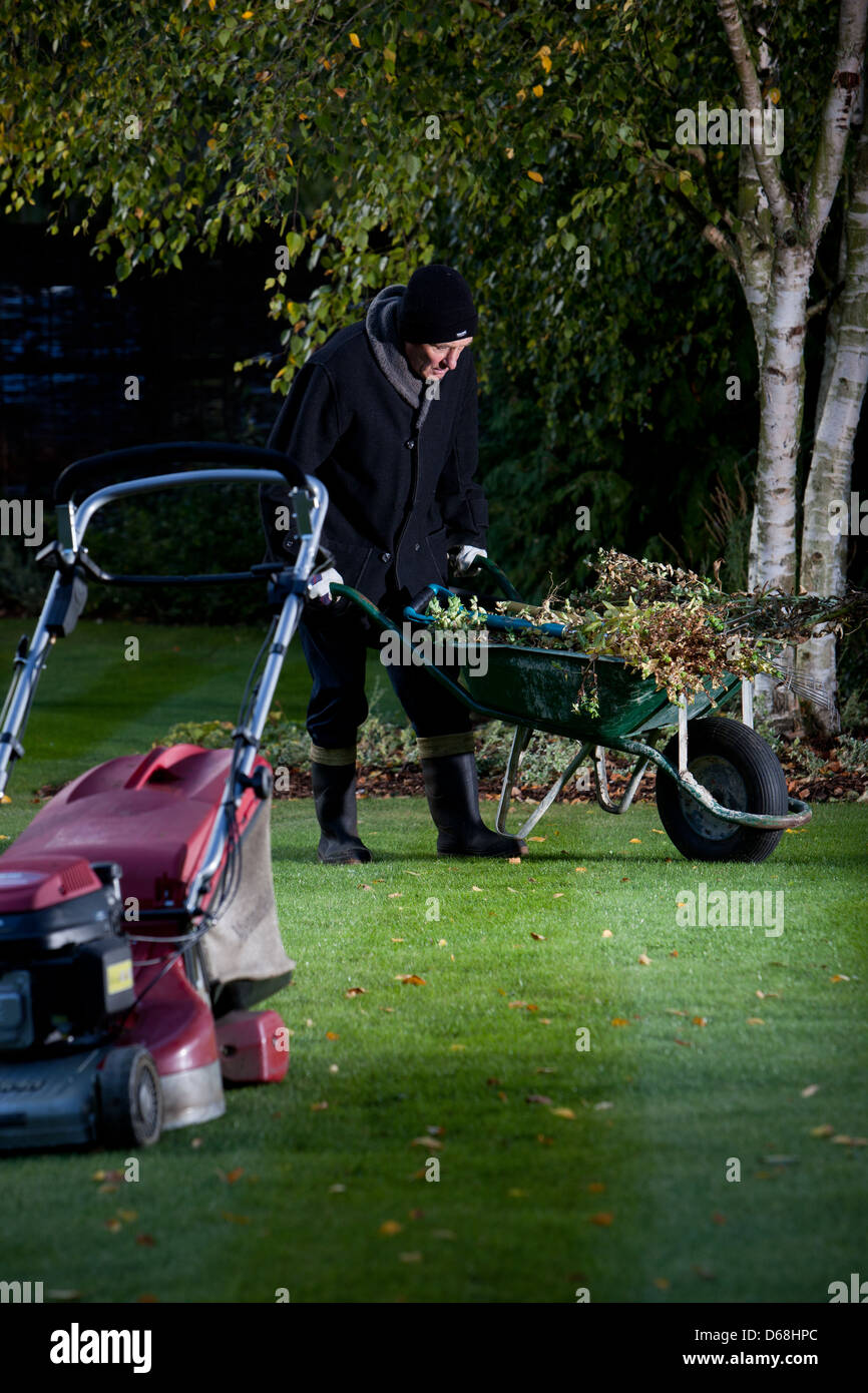 Alter Mann macht die Gartenarbeit, Schubkarre schieben, schneiden den Rasen. Stockfoto