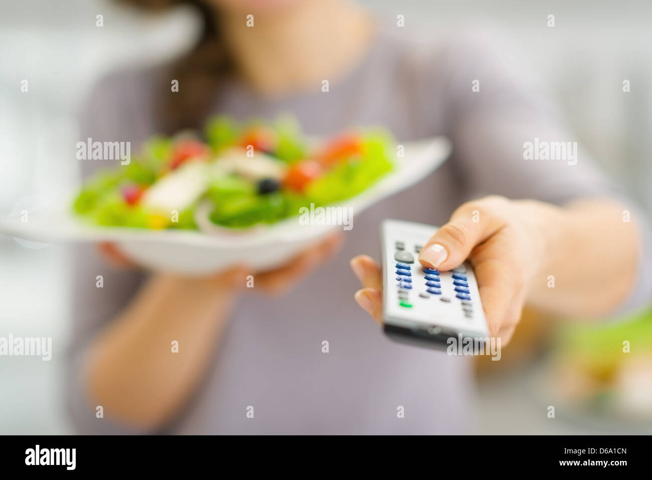 Closeup auf TV-Fernbedienung und frischem Salat in der Hand der jungen Frau Stockfoto