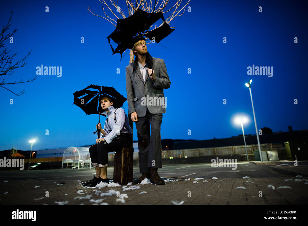 2 Schauspielern wie Vladimir & Estragon in klassischen Becketts "Warten auf Godot" spielen auf einem verlassenen Parkplatz nachts - warten auf Godot ist ein Theaterstück von Samuel Beckett, in denen zwei Zeichen, Vladimir und Estragon, auf die Ankunft von jemandem namens Godot, der nie ankommt warten, und warten sie engagieren in einer Vielzahl von Diskussionen und drei andere Figuren Stockfoto