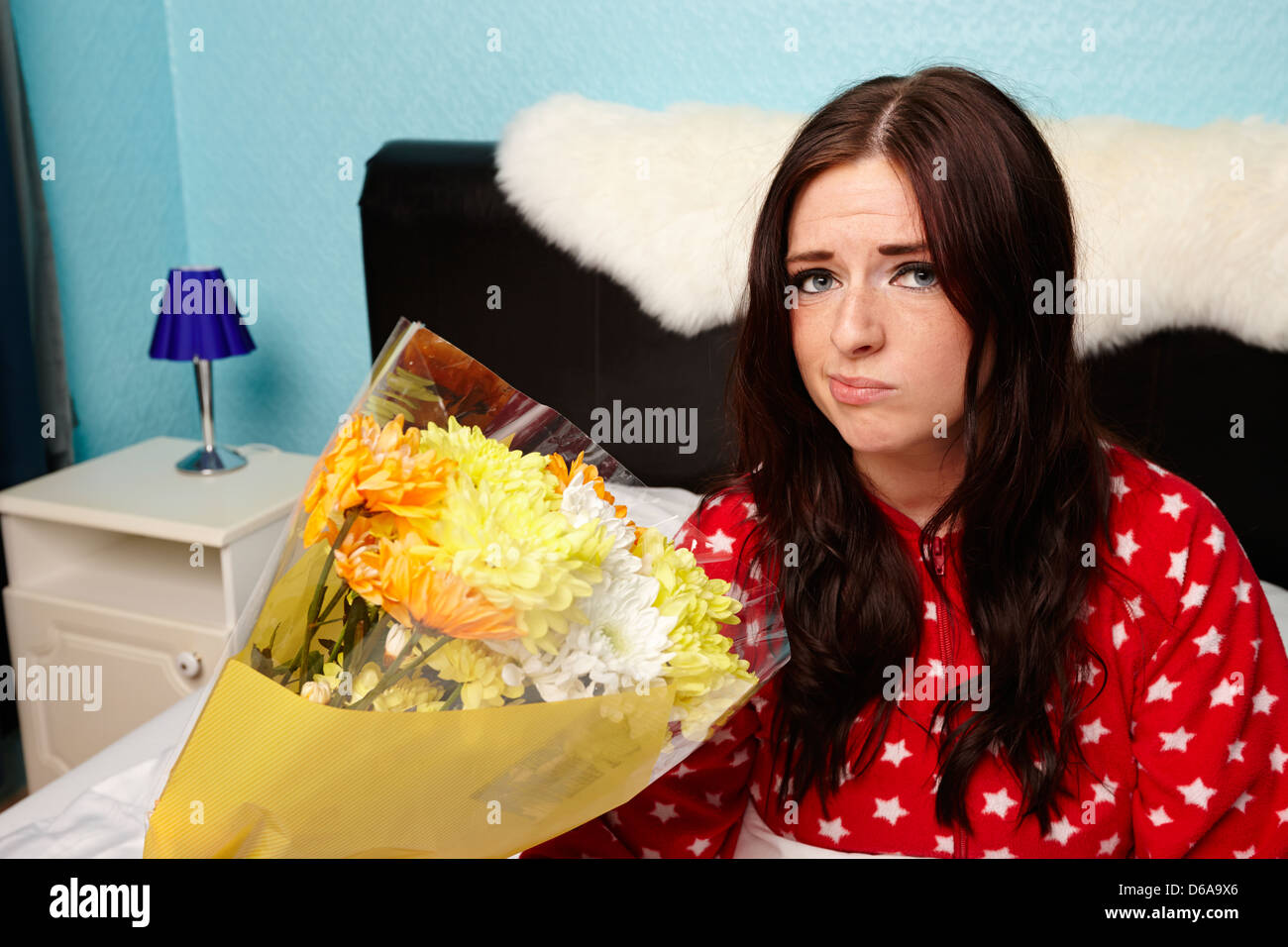 skeptische frühen zwanziger Jahren Frau mit Blumenstrauß im Bett in einem Schlafzimmer Stockfoto