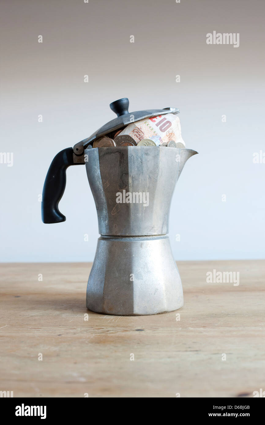 Kaffeekanne voller Geld auf Schreibtisch Stockfoto