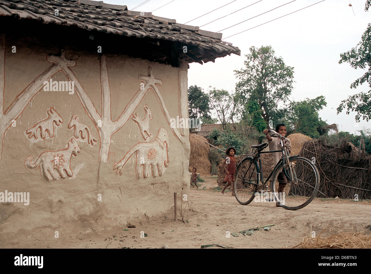 Haus mit einer typischen Wandmalerei in einem Dorf. Drei Kinder spielen auf der rechten Seite (Nepal) Stockfoto