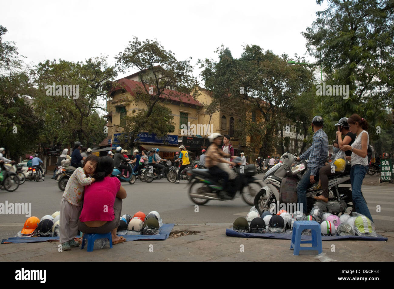 Horizontale Ansicht der Straßenhändler verkaufen Sturzhelme an belebten Kreuzung mit vielen Mopeds, Criss-crossing in alle Richtungen Stockfoto
