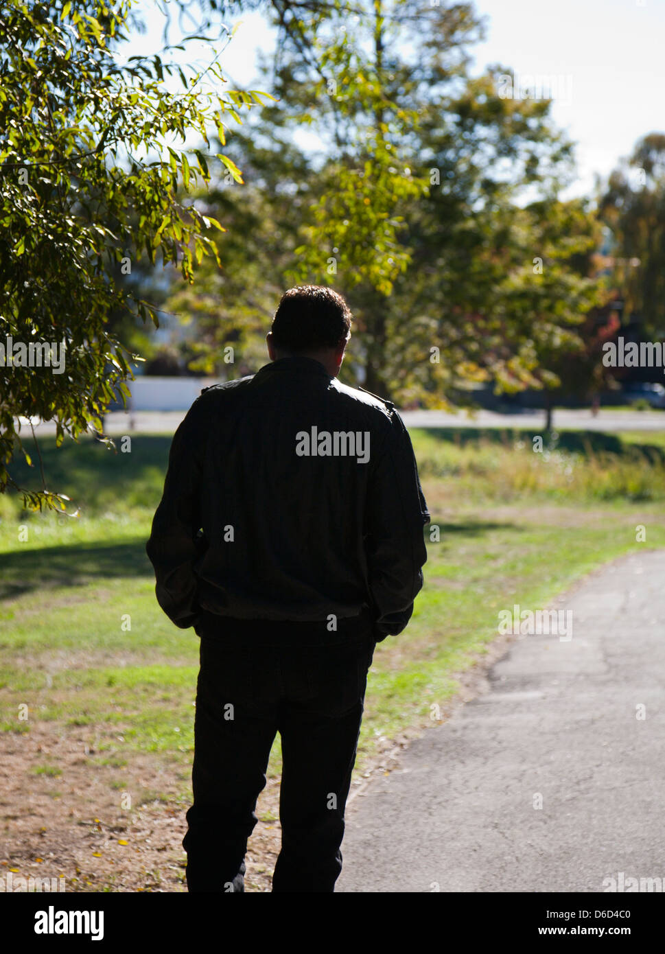Rückansicht eines Mannes, tief in Gedanken, allein zu Fuß entlang eines Pfads, Silhouette gegen einer ländlichen Umgebung. Stockfoto
