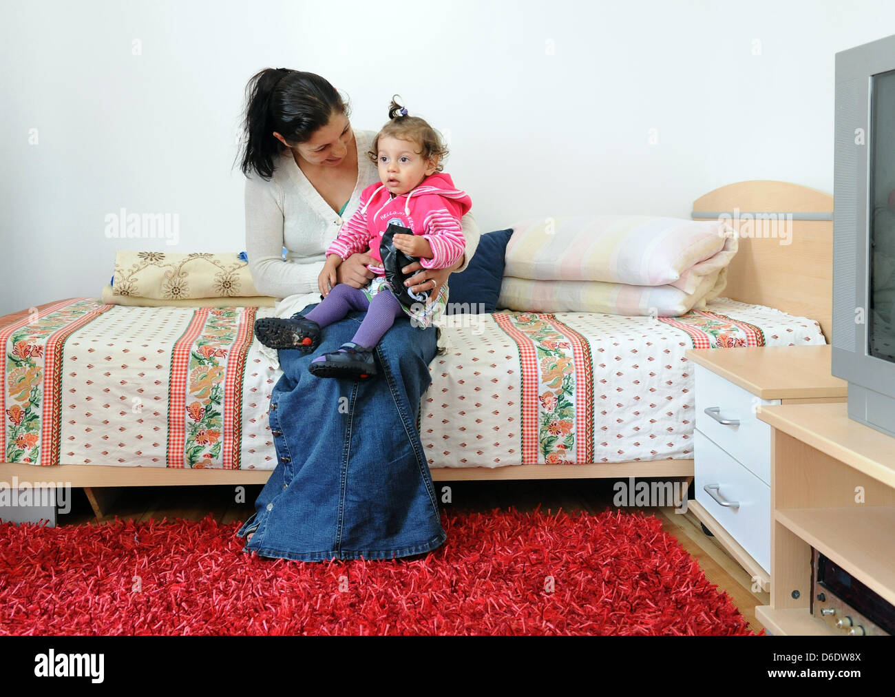 Doina sitzt auf einem Bett hält ihr Baby im Arm in ihrer Wohnung befindet sich in einem Mehrfamilienhaus in der Harzer Straße in Berlin, Deutschland, 14. September 2012. 500 Roma aus Rumänien wird in 137 renoviert und bezahlbare Wohnungen in naher Zukunft bewegen. Das Wohnprojekt wurde initiiert von der Aachener Siedlungs - Und Wohnungsbaugesellschaft (Aachener Siedlungs- und Wohnungsbau Association), wh Stockfoto