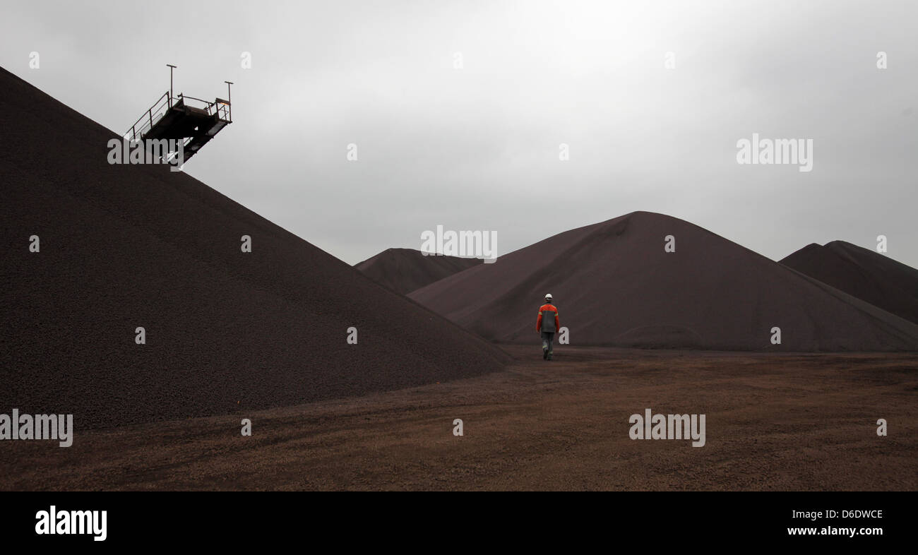 Ein Mitarbeiter geht vorbei an verschiedenen Haufen Eisen-Erz-Pellets auf einem Lagerplatz in der ArcelorMittal Stahl-Fabrik in Hamburg, Deutschland, 14. September 2012. Der weltweit größte Stahlkonzern zählt im laufenden Jahr auf einem zusätzlichen Abschwung von zwischen drei und fünf Prozent in Europa. Angesichts des weltweiten Wettbewerbs auf dem Stahlmarkt sind die hohen Energiekosten Cauing co Stockfoto