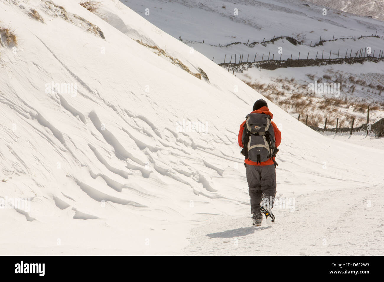 Eine Walker übergibt massive Schneeverwehungen blockieren die Kirkstone Pass-Straße über Ambleside Stockfoto