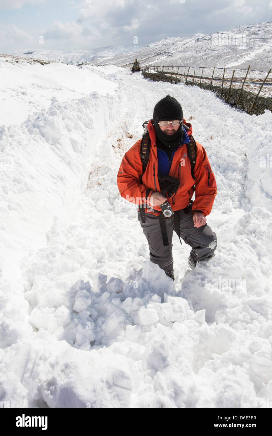 Eine Walker steht neben massiven Schneeverwehungen blockieren die Kirkstone Pass-Straße über Ambleside Stockfoto