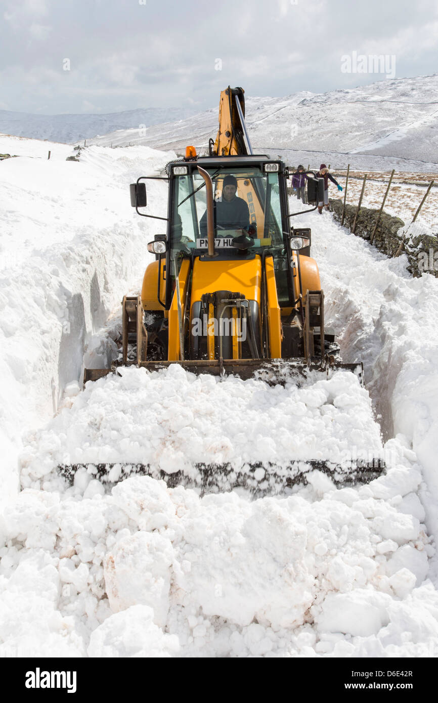Ein JCB versucht, einen Weg durch massive Schneeverwehungen blockieren den Kirkstone Pass löschen Stockfoto