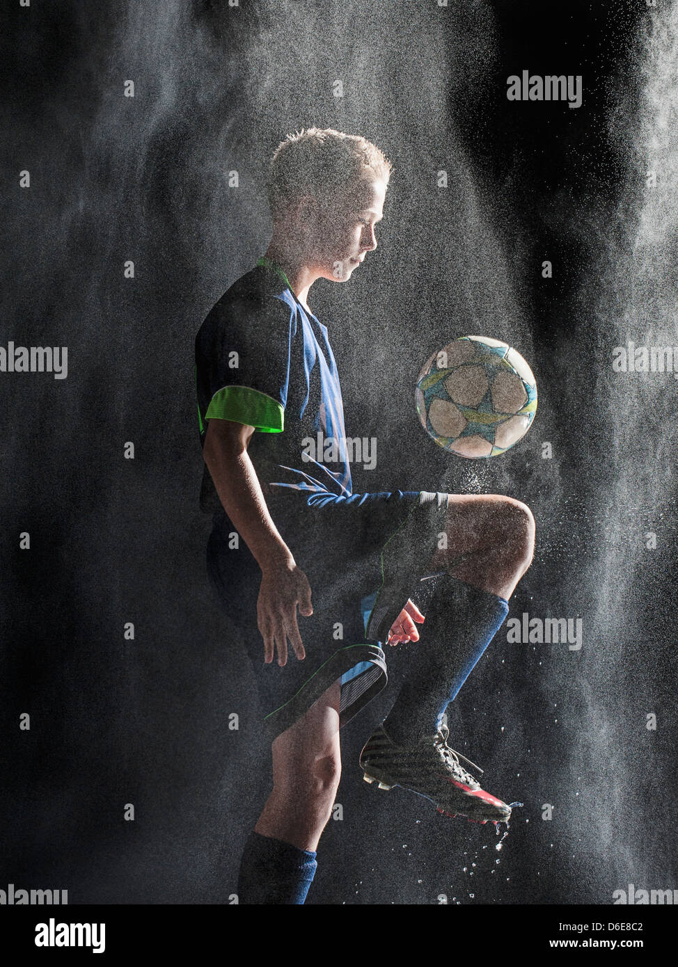 Kaukasische Fußballspieler treten Ball im Regen Stockfoto