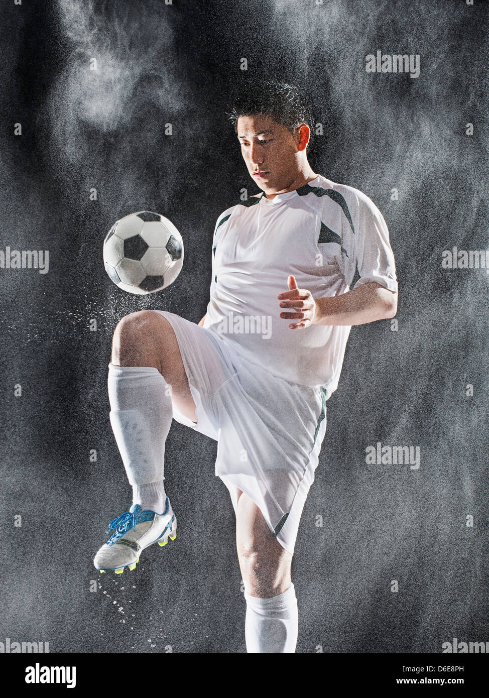 Asiatische Fußball-Spieler treten Ball im Regen Stockfoto