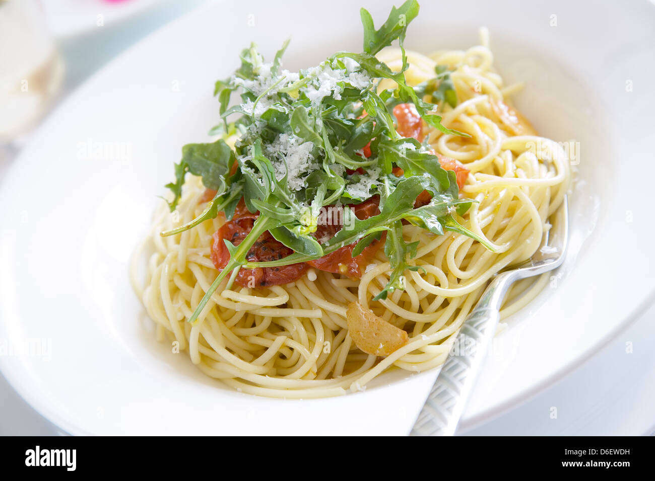 Spaghetti mit Olivenöl, garniert mit gerösteten Tomaten, Knoblauch, Zwiebel und Rucola Stockfoto