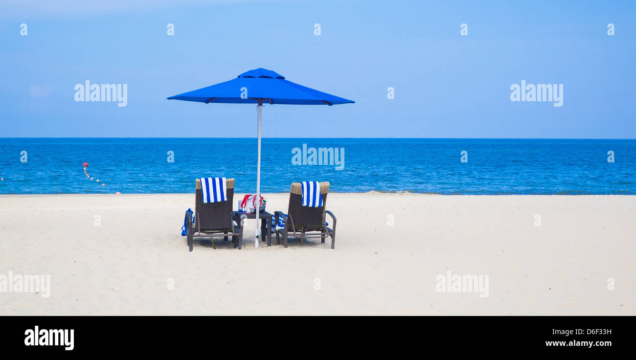Strand und blauen Meer mit blauen Sonnenschirm zwei Sonnenliegen und blau gestreiften Handtüchern Borneo Sabah Malaysia Stockfoto