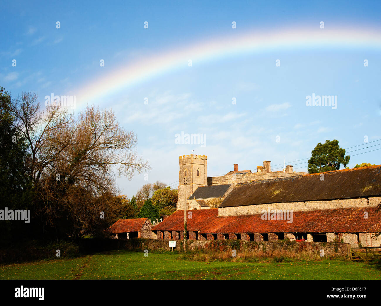 Regenbogen über der Kirche Herrenhaus und Wirtschaftsgebäuden des East Quantoxhead in Somerset UK Stockfoto