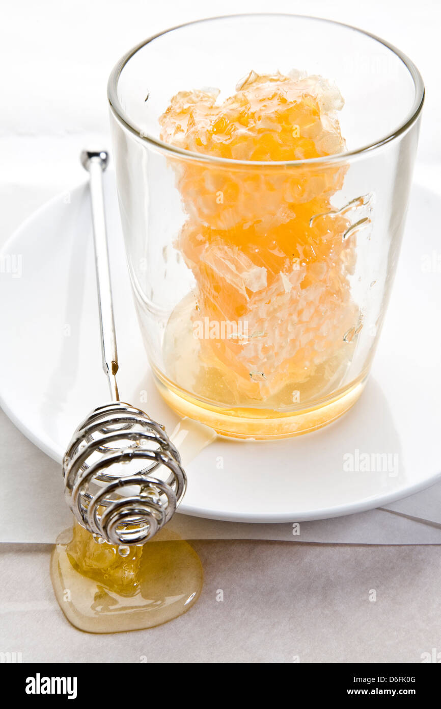 Ein Glas gefüllt mit süßen Wabe Honig nieselte aus einen Honig-Stab auf weißem Pergament-Papier Stockfoto