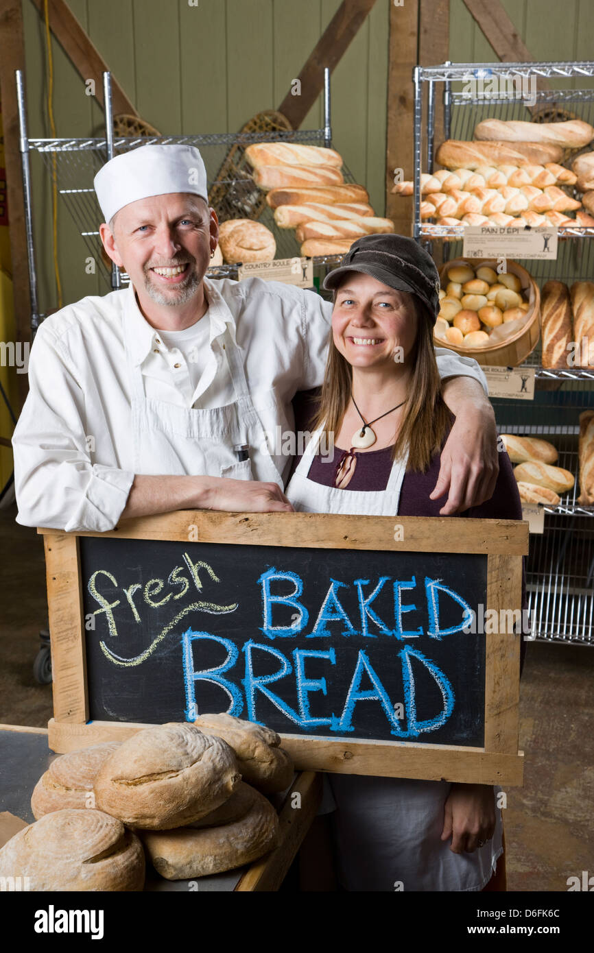 Porträt von Mann und Frau-Team in ihren kommerziellen Bäckerei, umgeben von frisch gebackenem Brot Stockfoto