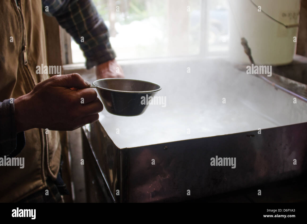 Bio-Landwirt skimming Verunreinigungen aus kochendem Ahorn Sap mit der hand während des Prozesses der Herstellung von Ahornsirup. Stockfoto