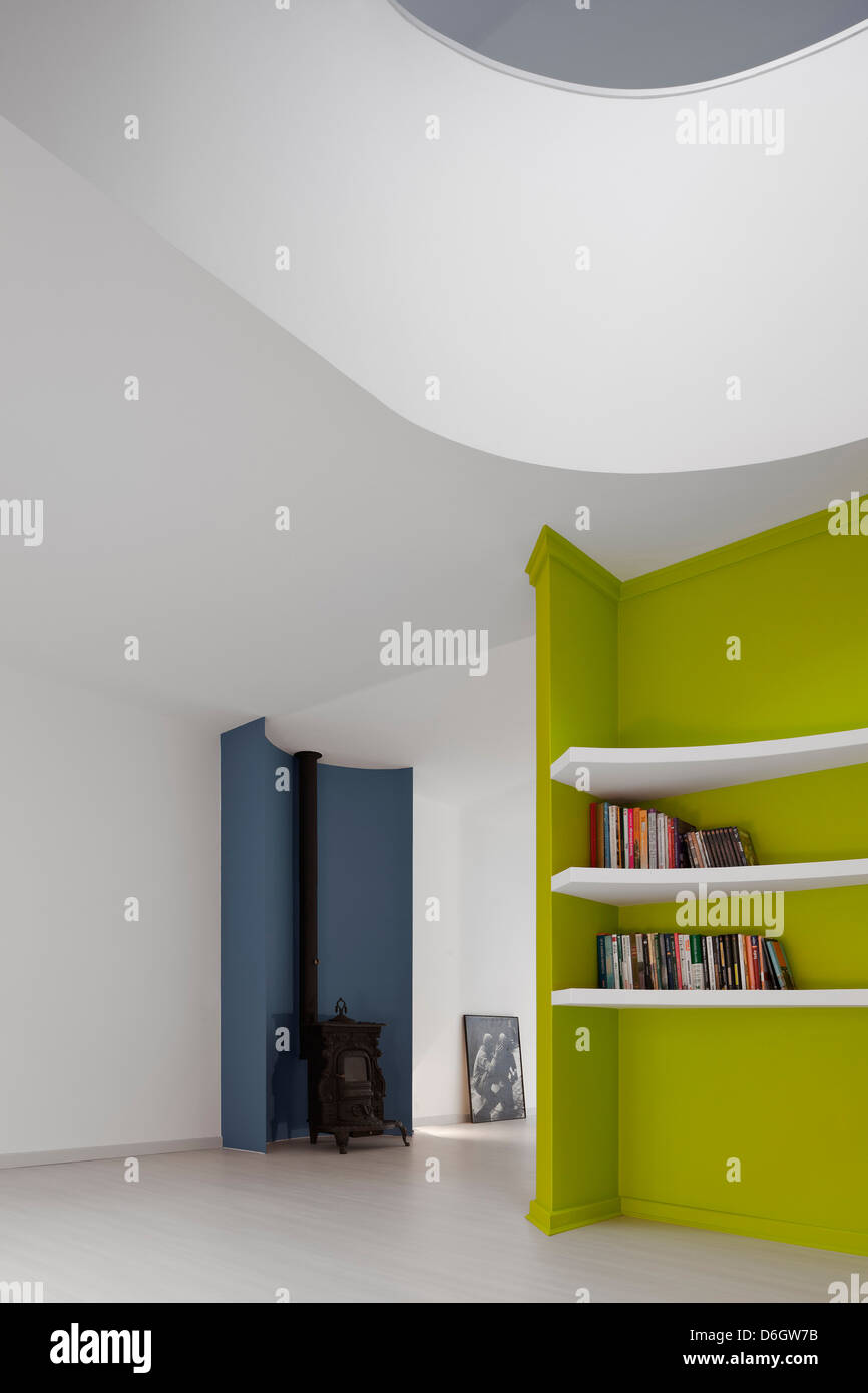 Casa Em Almada, Almada, Portugal. Architekt: Pedro Gadanho, 2012. Lebenden Bereich Ansicht mit Kalk farbig Bücherregal und Holzofen. Stockfoto