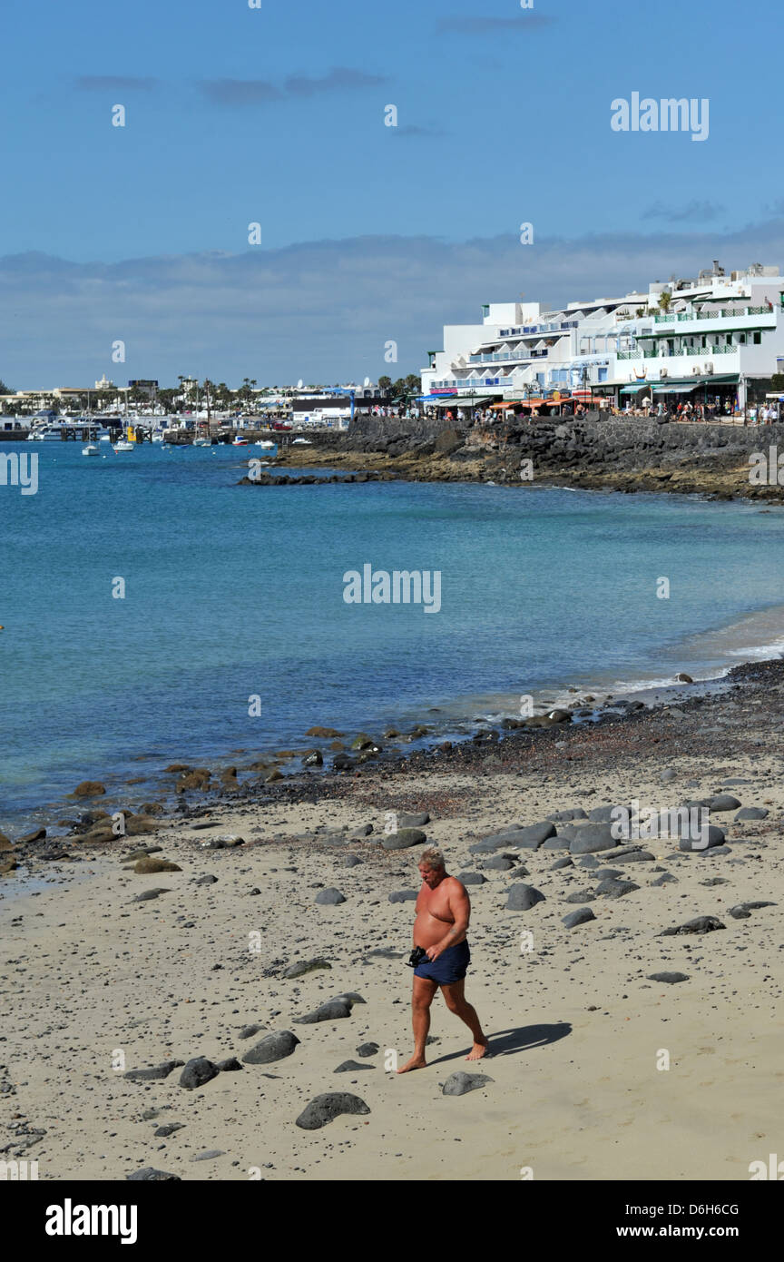 Ein großer Mann, das Tragen von Badeshorts Spaziergänge am Strand in Playa Blanca, Lanzarote, Kanarische Inseln. Stockfoto