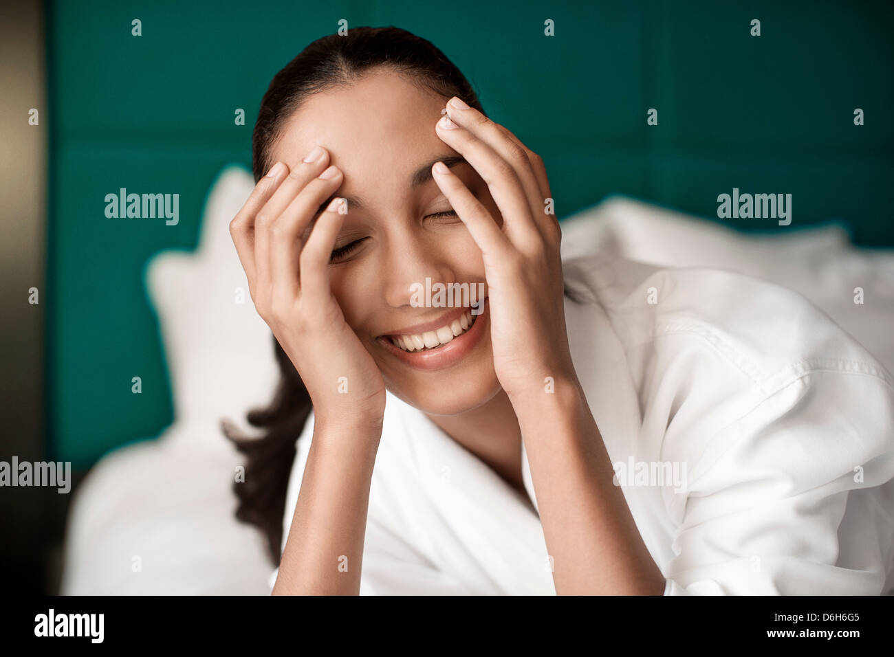 Frau im Bademantel lächelnd auf Bett Stockfoto