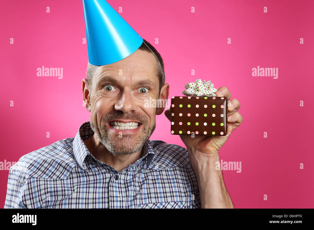 Mann trägt einen Partyhut mit einem großen toothy Lächeln und hält ein Geschenk. Stockfoto