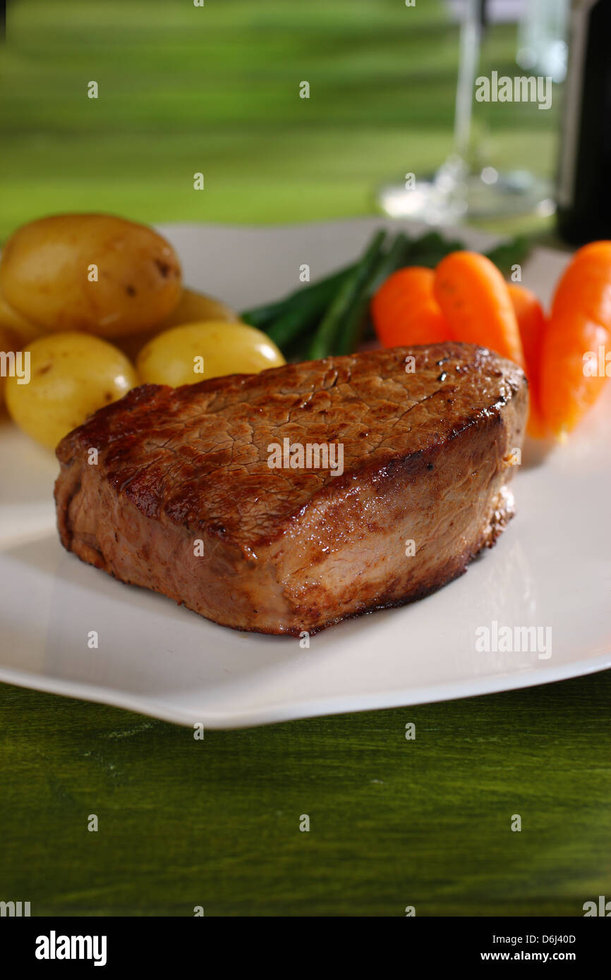 Filet Steak Rind Madellion mit Karotten, grüne Bohnen und Babykartoffeln auf einem weißen Teller & grünen Hintergrund Stockfoto