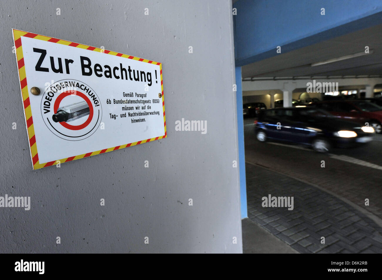 Ein Auto fährt vorbei an einem Schild Videoüberwachung in Emden, Deutschland, 30. März 2012 angekündigt. Dahinter befindet sich ein Banner-Werbung Zivilcourage. Ein 11 Jahres altes Mädchen wurde tot in einem Notausgang Bereich eines Parkhauses in Emde am 24. März 2012 gefunden. Die 17-jährige Mordverdächtigen wurde aus der Untersuchungshaft am Freitag entlassen. Die Möglichkeit, dass er der Täter war kann ausgeschlossen werden, Accoring t Stockfoto