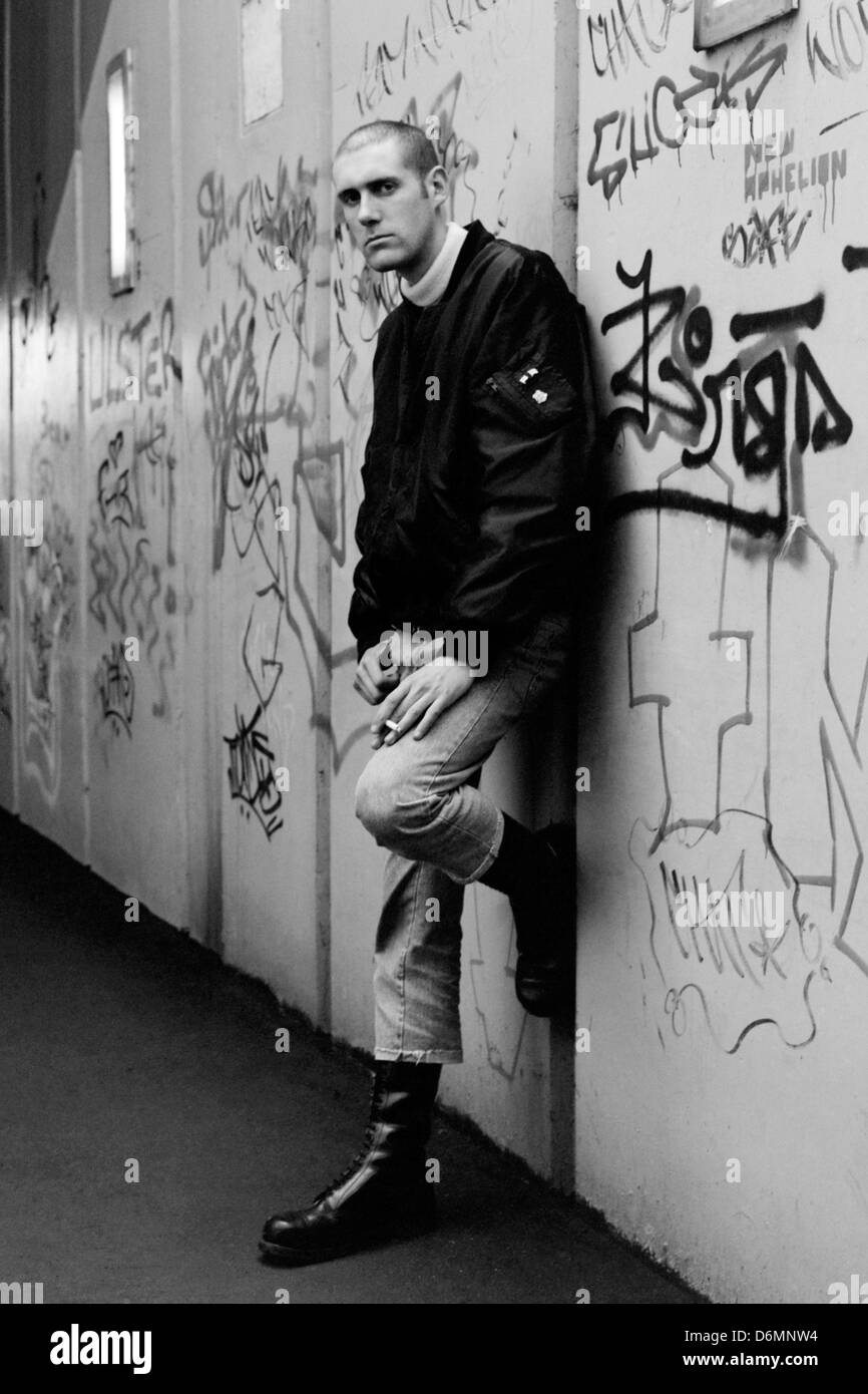 Junger männlicher Skinhead, der in einem Graffiti steht, das schwach