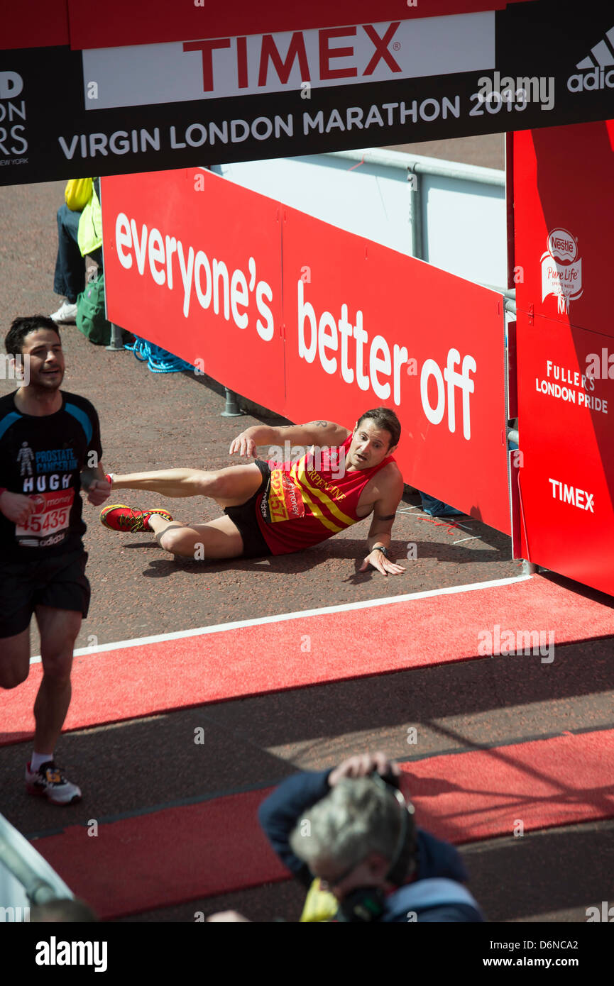 Ein Läufer zusammenbricht und kriecht über die Ziellinie des 2013 Virgin London Marathon in The Mall. Stockfoto