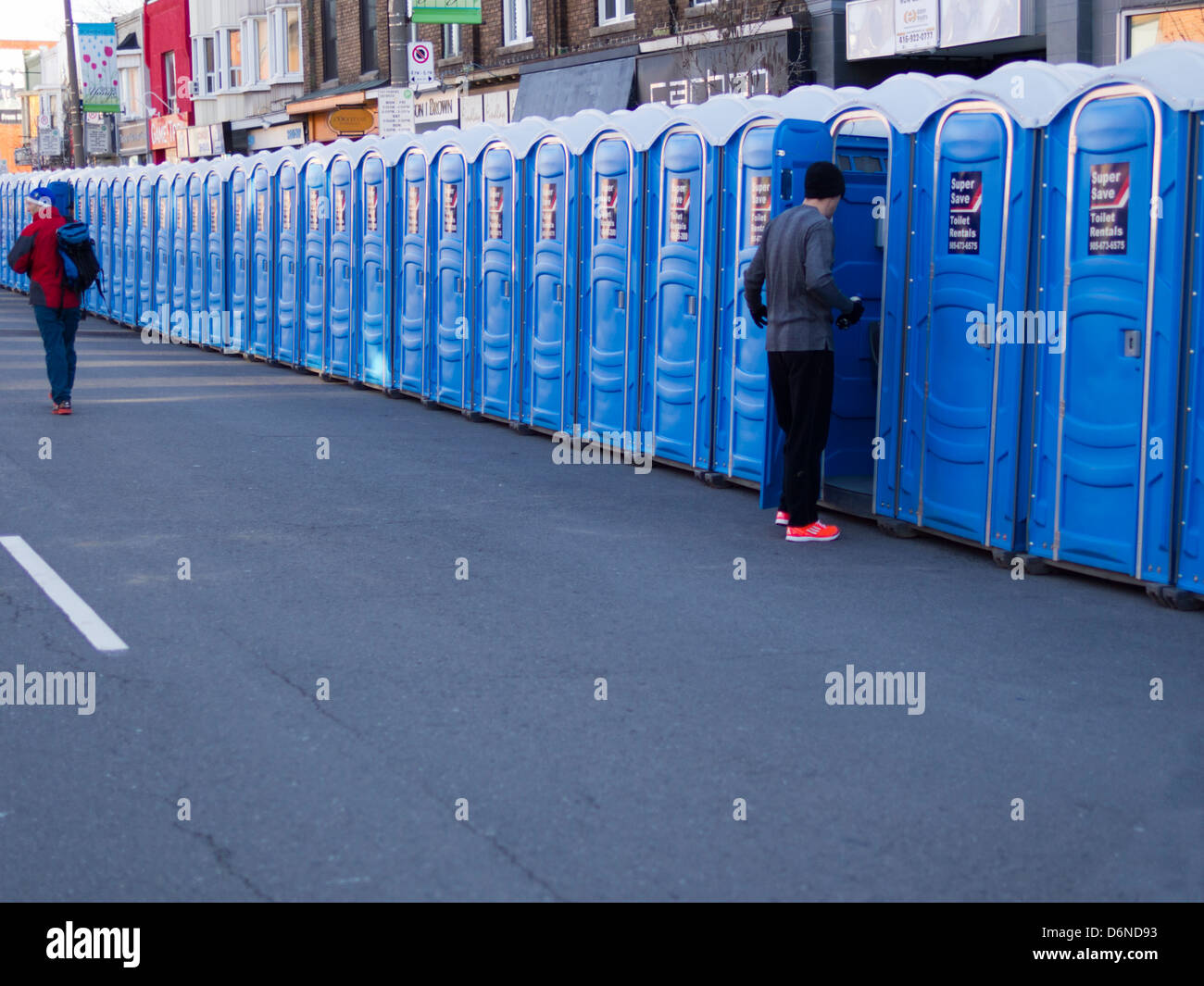 Eine Person betritt eine tragbare Toilette, während andere entlang des Ufers von mobilen Toiletten an der Toronto Yonge Street 10 K laufen Spaziergänge Stockfoto