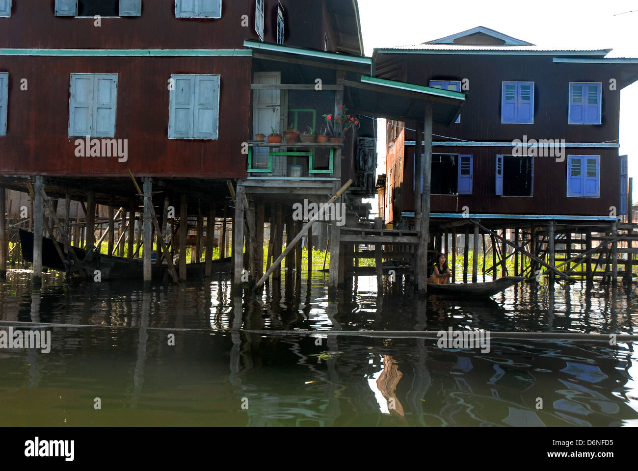 Traditionelle Myanmar Inle-See, Gebäude, gebaut auf Pfählen über dem Wasser mit jungen Mädchen sitzen im Boot unter Haus Stockfoto