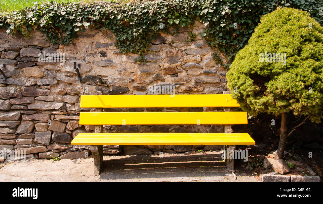 leuchtend gelbe Parkbank vor einer Steinmauer Stockfoto