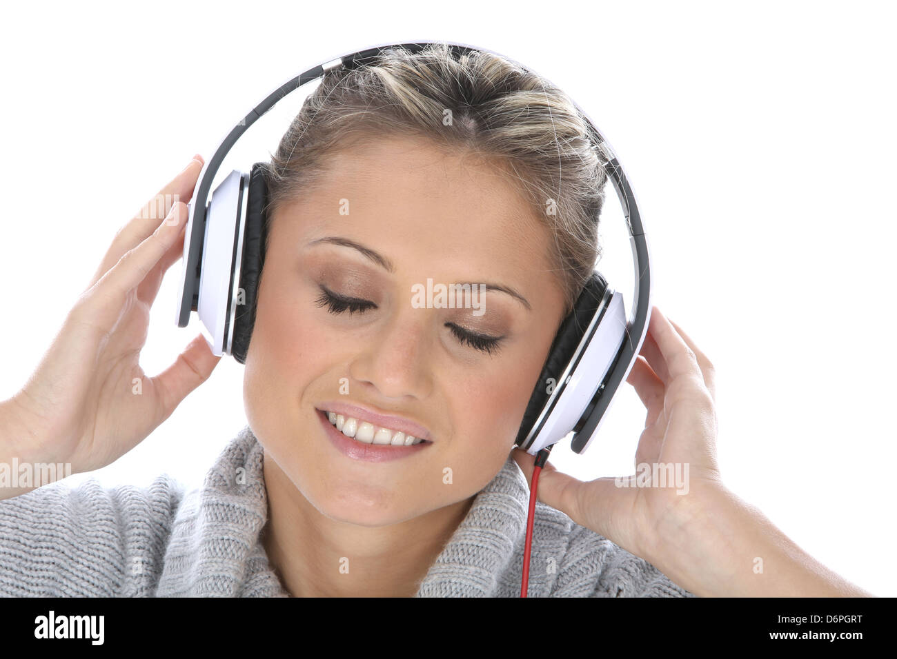 Attraktive junge Frau mit Kopfhörern und genießen Sie Musik hören vor einem weißen Hintergrund mit Blickkontakt zur Kamera zu lächeln und glücklich Stockfoto
