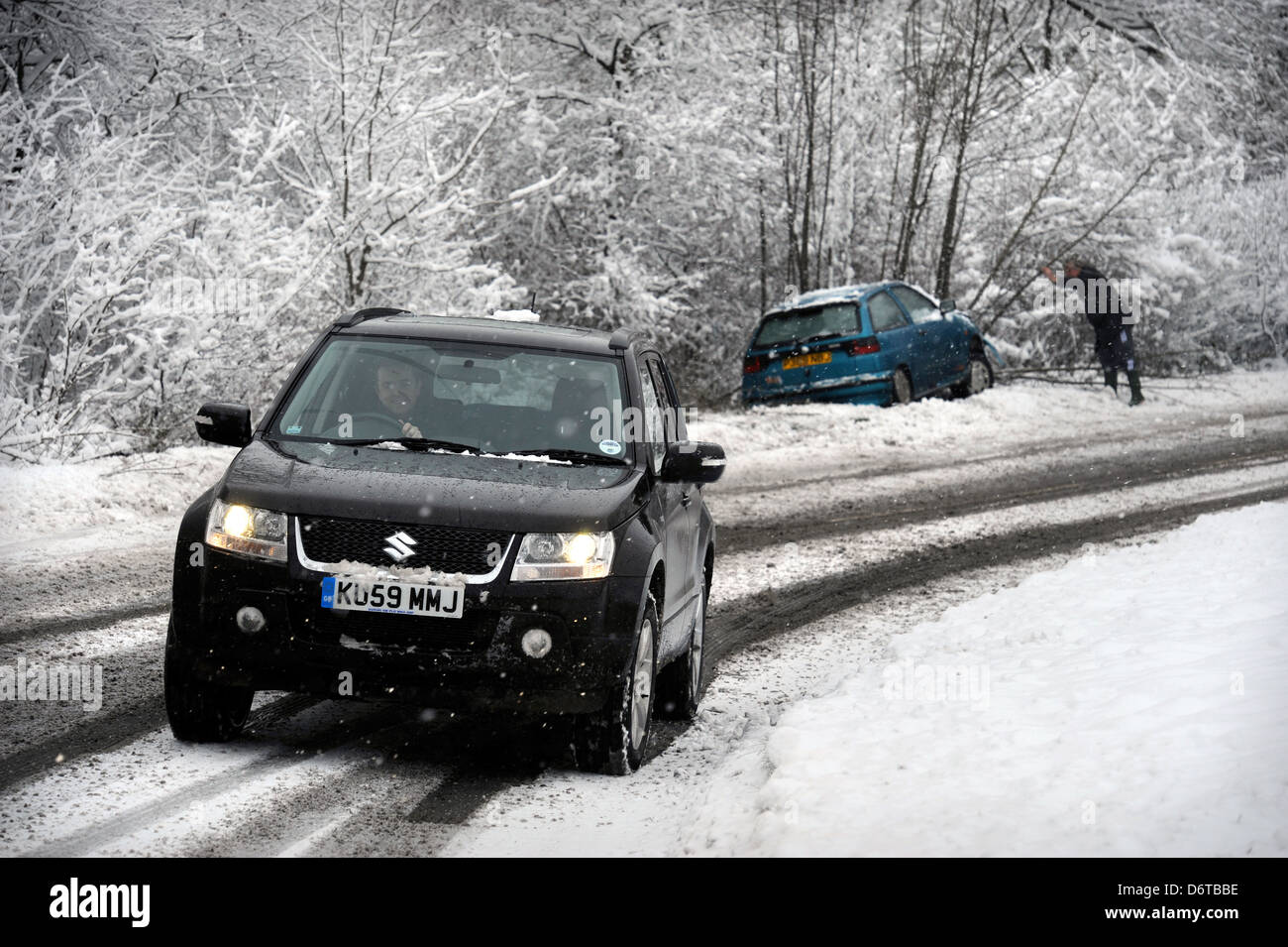 Ein 4 x 4 Fahrzeug fährt ein abgestürztes Auto, das die Strasse in den schneebedeckten Bedingungen in der Nähe von Stroud Gloucestershire UK links Stockfoto