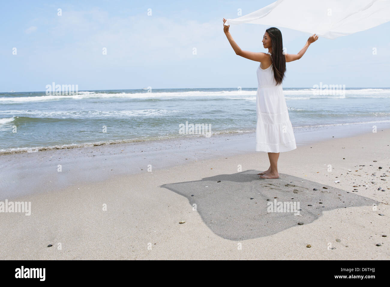 Frau in einem weißen Kleid mit weißen Tuch am Strand Stockfoto
