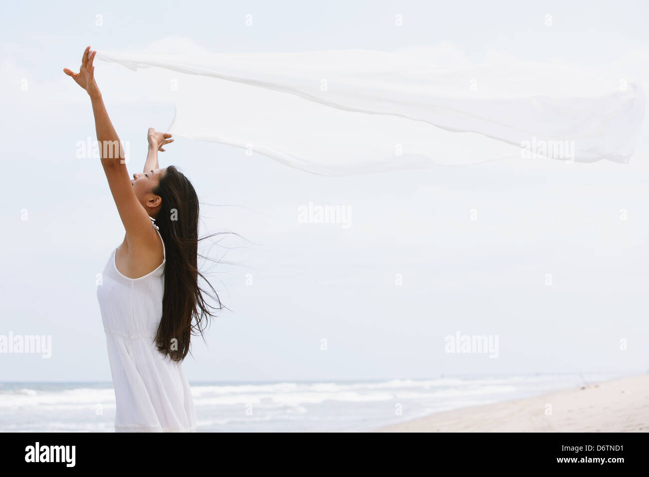 Frau in einem weißen Kleid mit weißen Tuch am Strand Stockfoto