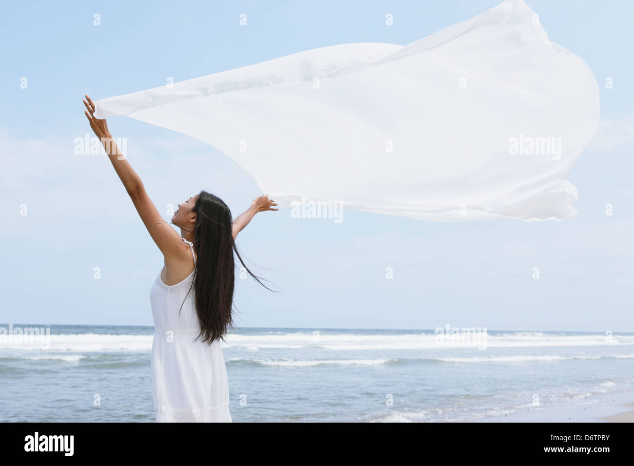 Frau in einem weißen Kleid mit weißen Tuch am Strand Stockfoto