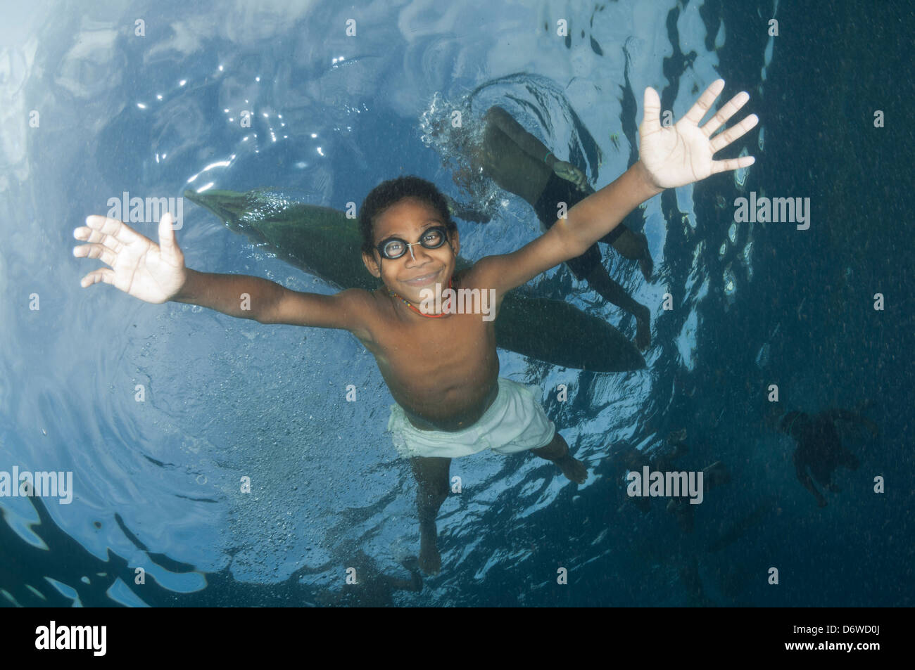 Ein kleiner Junge schwimmt unter seinem Kanu und lächelt für Taucher unten Stockfoto