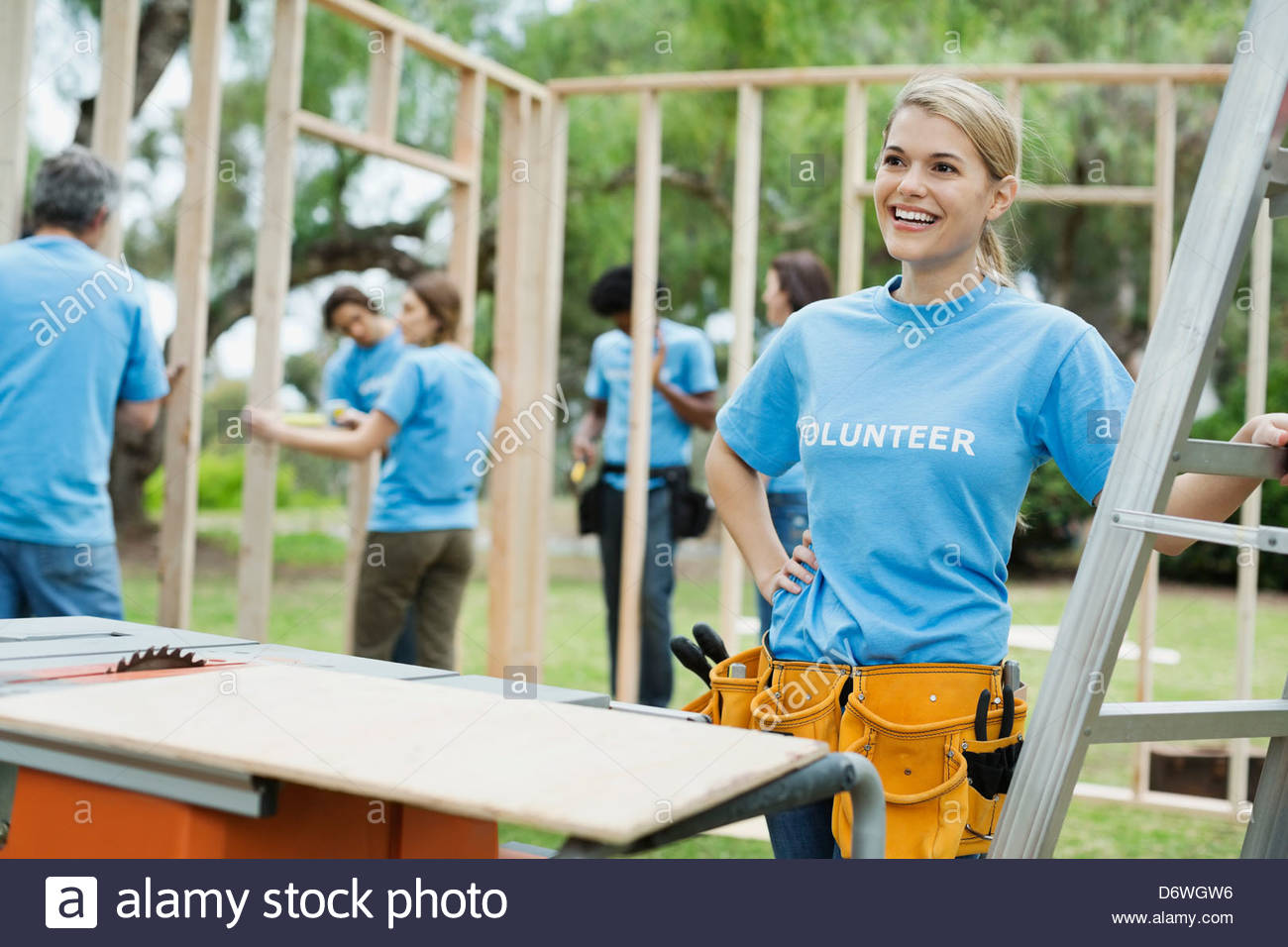 Glückliche junge Frau Leiter mit Freiwilligen Gebäude Holzrahmen im Hintergrund Stockfoto