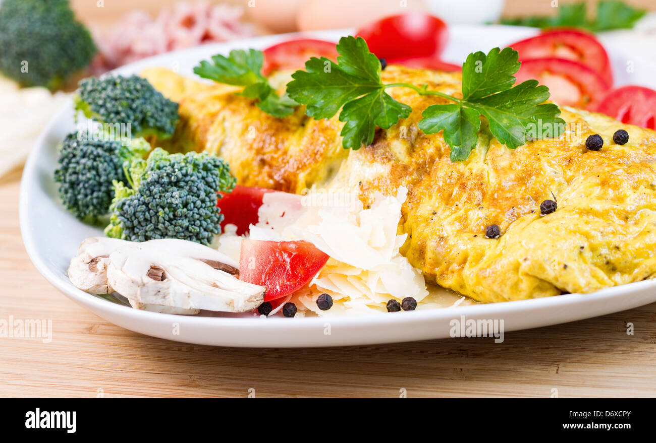 Horizontale Foto großes Ei Omelett mit Champignons, Käse, Broccoli, Tomatenscheiben, Pfeffer und Petersilie in weißer Teller Stockfoto