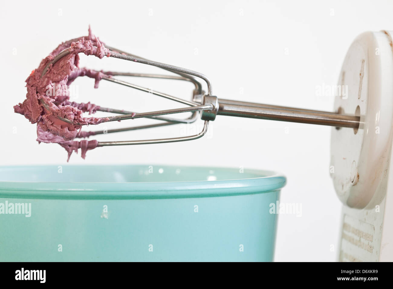 elektrischen Mixer mit rosa/roten Zuckerguss auf den Schläger mit einer blauen Schüssel, Stockfoto
