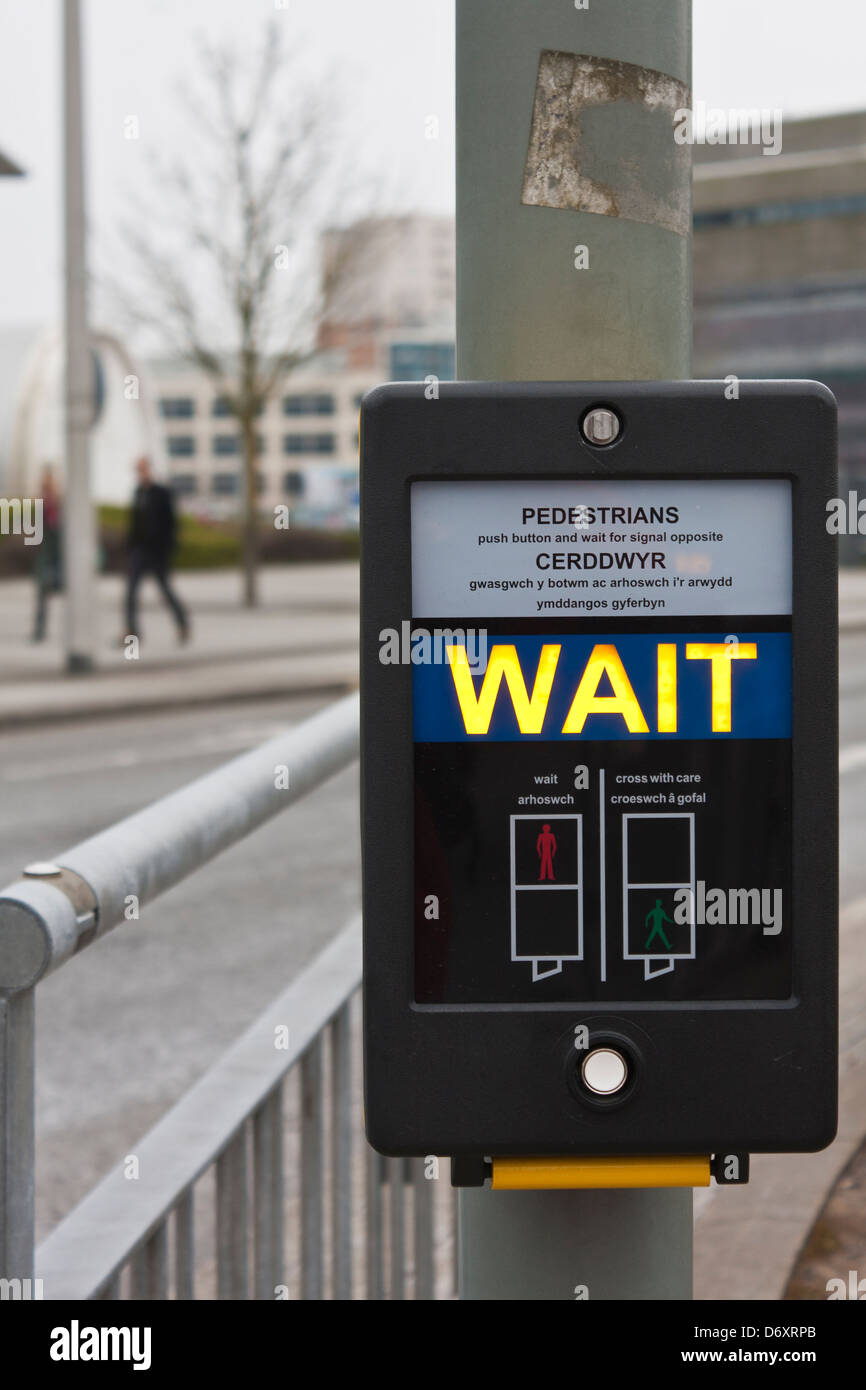 Fußgänger warten Schild am Pelican Crossing in den Sprachen Englisch und Walisisch. Stockfoto