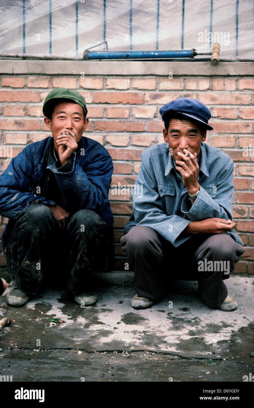 Zwei Männer, die das Rauchen von Zigaretten beim hocken auf dem Bürgersteig, China Stockfoto