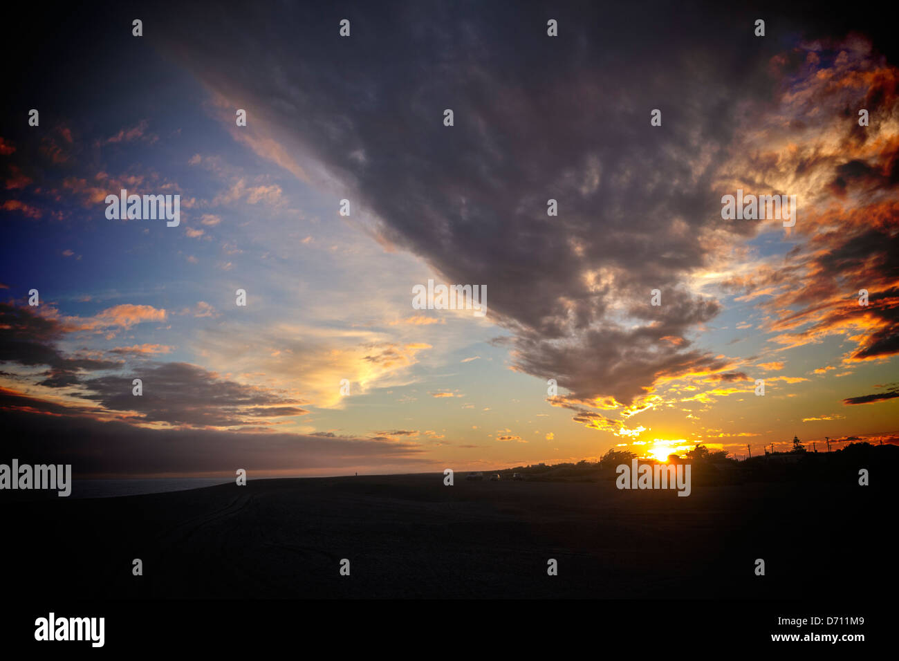 Sonnenuntergang in Moody Himmel - dramatischen Sonnenuntergang über einem dunklen Strand. Stockfoto